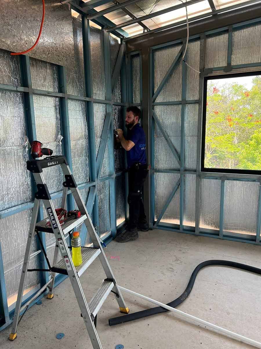 A Man Is Insulating A Wall In A Room With A Ladder — COOLIT NT In Berry Springs, NT