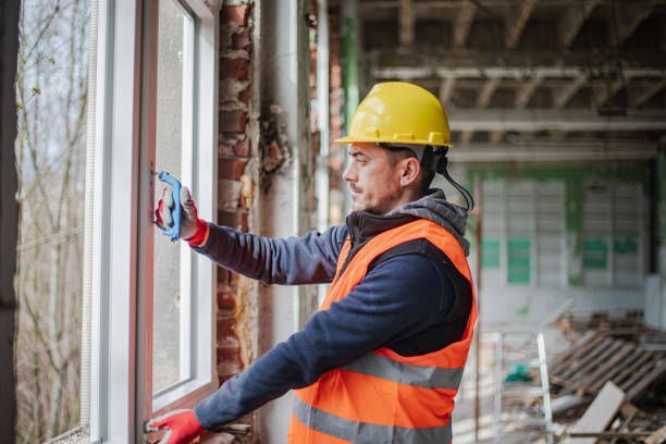 Construction worker in safety gear installing a window frame in a building.