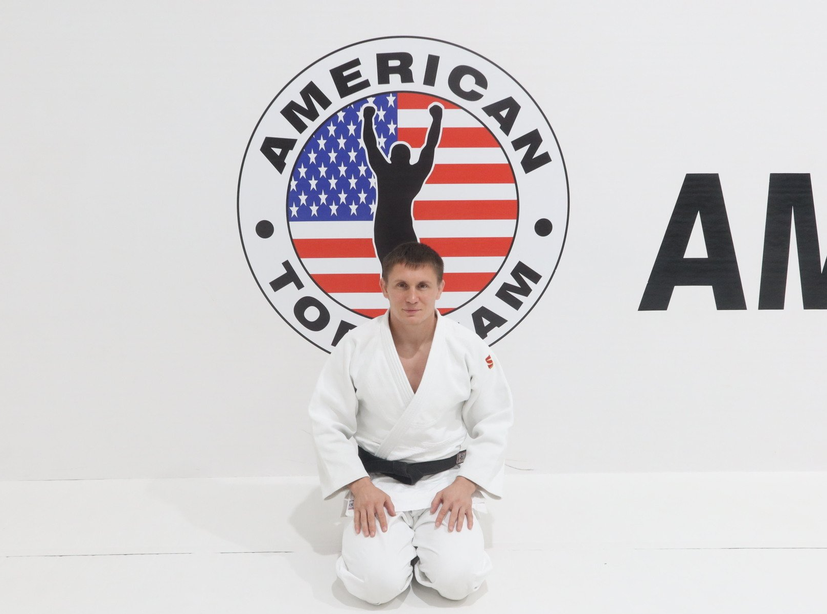 Arthur Tsyar kneeling in front of the American Top Team Logo