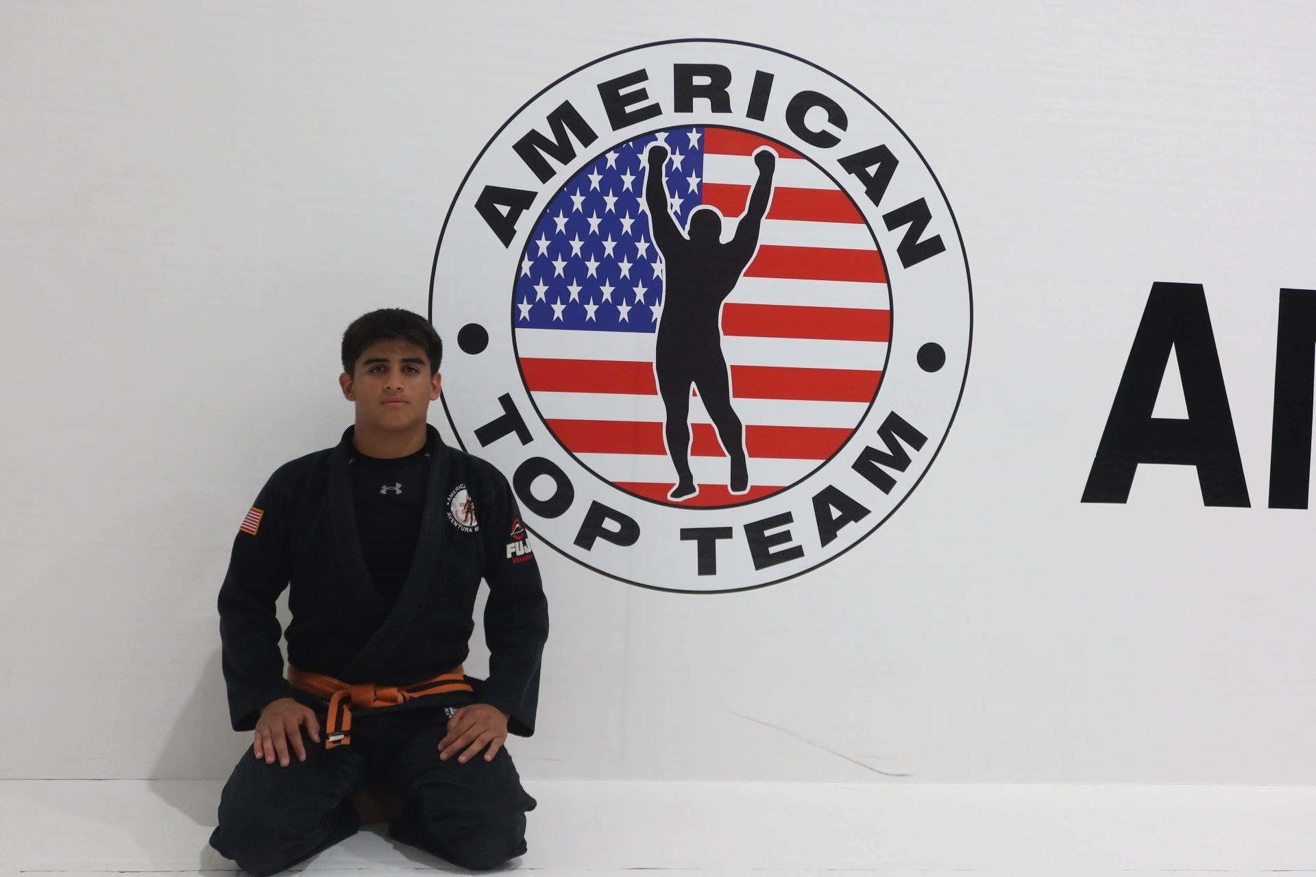 Darius Calderon kneeling in front of American Top Team Logo