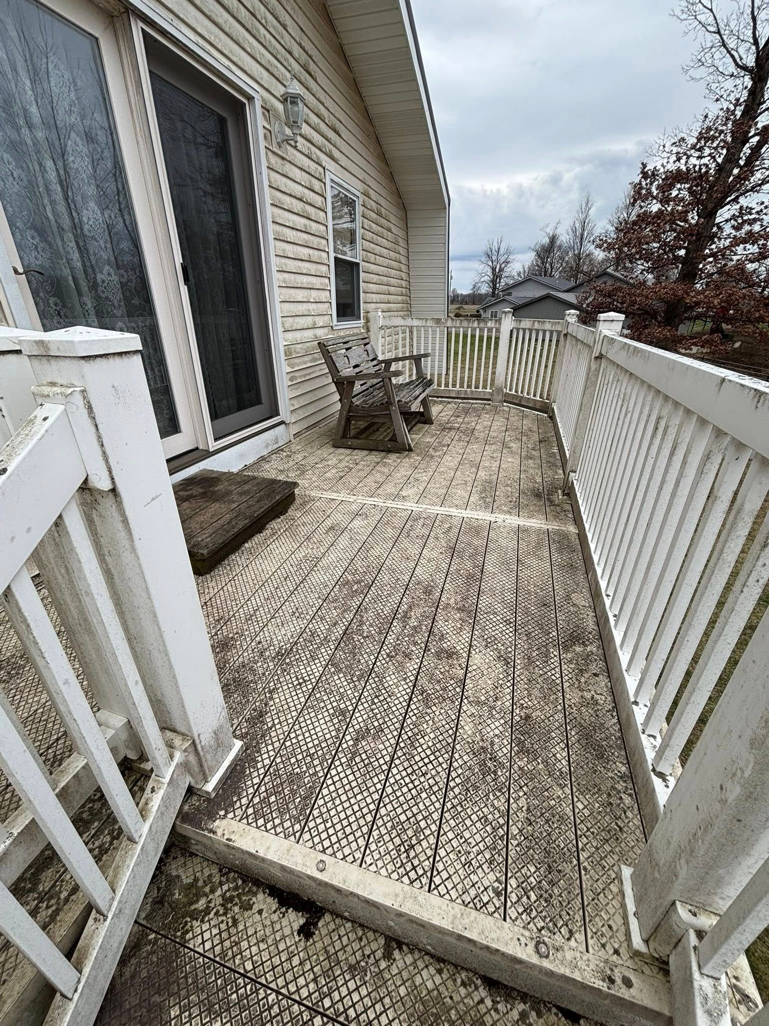 A dirty porch with a white fence and chairs on it next to a house.