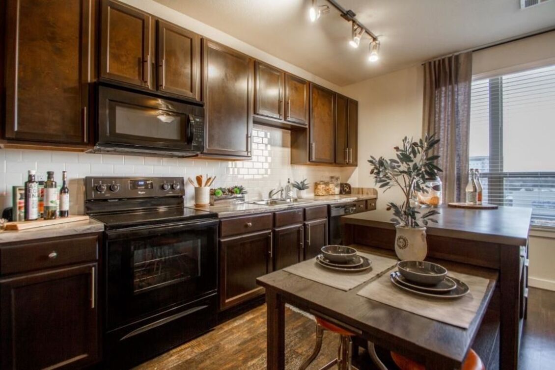 A kitchen with brown cabinets , black appliances , a table and chairs at Park Avenue Lofts.