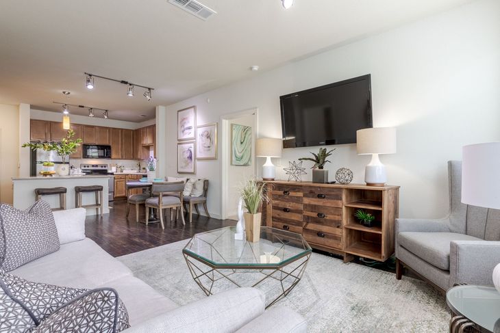 Modern living room with open kitchen and dining area, wood accents, and neutral tones.