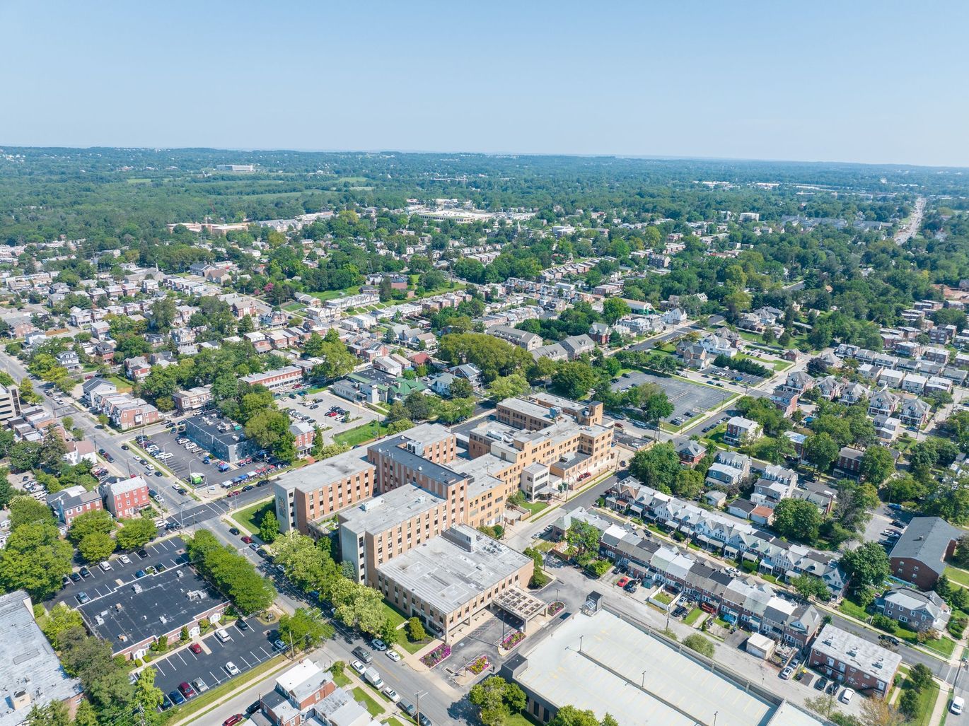 Aerial view of a residential area with a large multi-story building and surrounding trees under a clear sky.