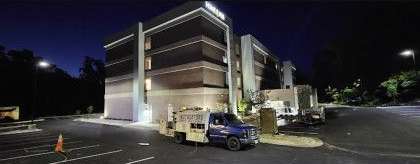 Exterior of a modern building at night. A work truck is parked out front, with a dark sky above.
