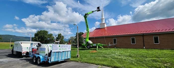 A green lift reaches the steeple of a brick church; trucks are in the foreground on a sunny day.