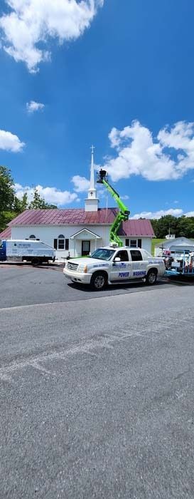 White building with red roof, workers on a lift, blue sky with clouds, white truck parked in front.