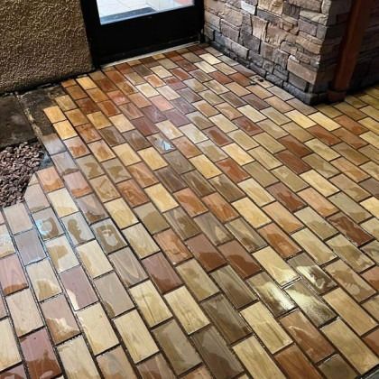 Wet brick patio entrance with varied shades of brown and tan, next to stone wall and door.