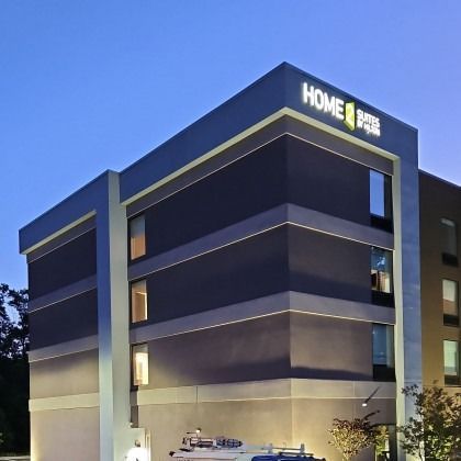 Home2 Suites by Hilton hotel exterior at dusk. Gray and dark grey building with lit windows.