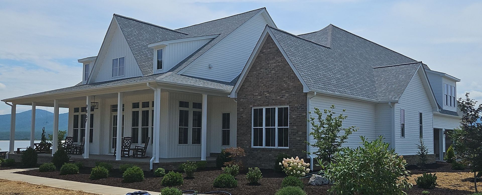 White farmhouse with a porch and a brick chimney under a blue sky.
