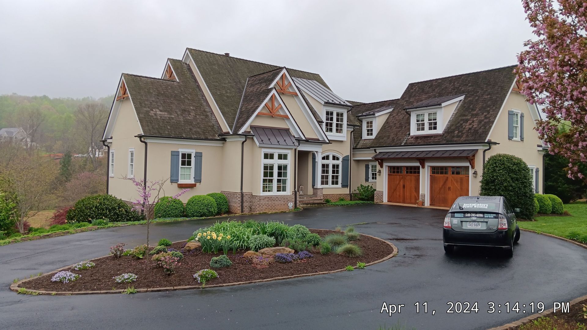 House with a circular driveway; tan stucco, brown roof, and garage doors; car in drive.