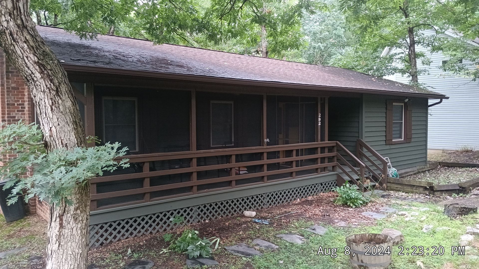 A weathered, green cabin with a screened porch in a wooded area.