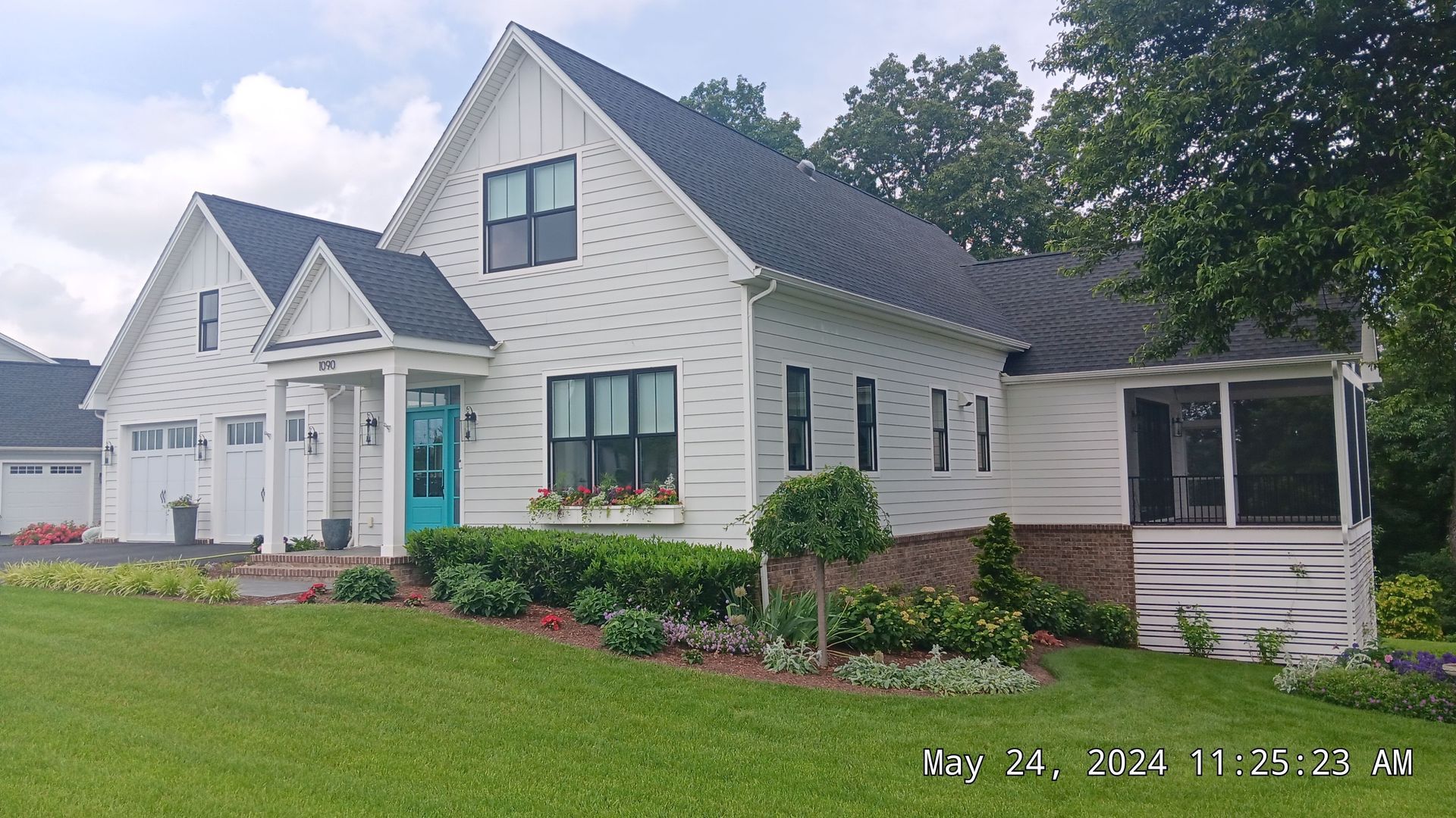 White house with black roof, teal door, and screened porch on green lawn.