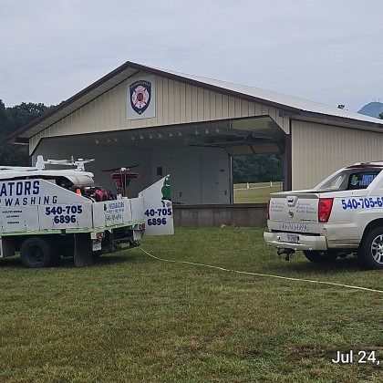 A white truck towing a white pickup truck on a grassy field in front of a tan building.