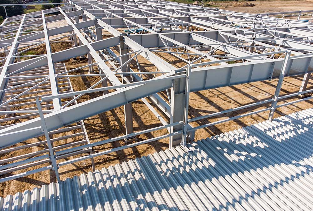 Steel framework of a building under construction, viewed from above, casting long shadows on corrugated roofing.