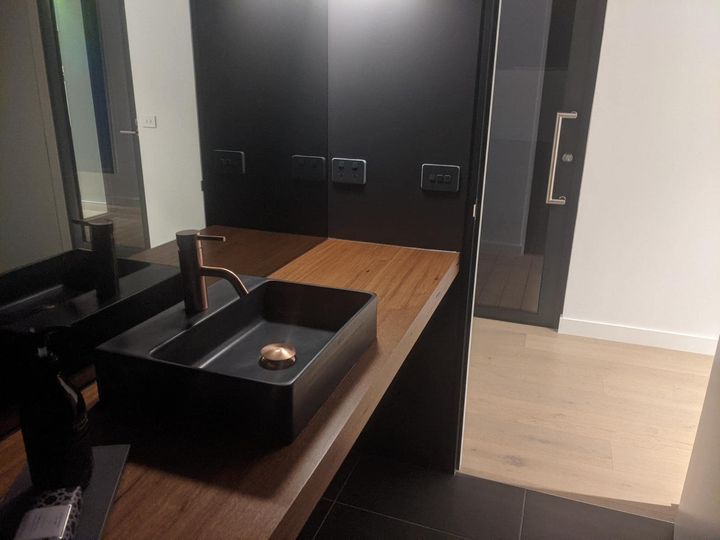 Modern bathroom vanity with black sink and tap on wooden countertop.