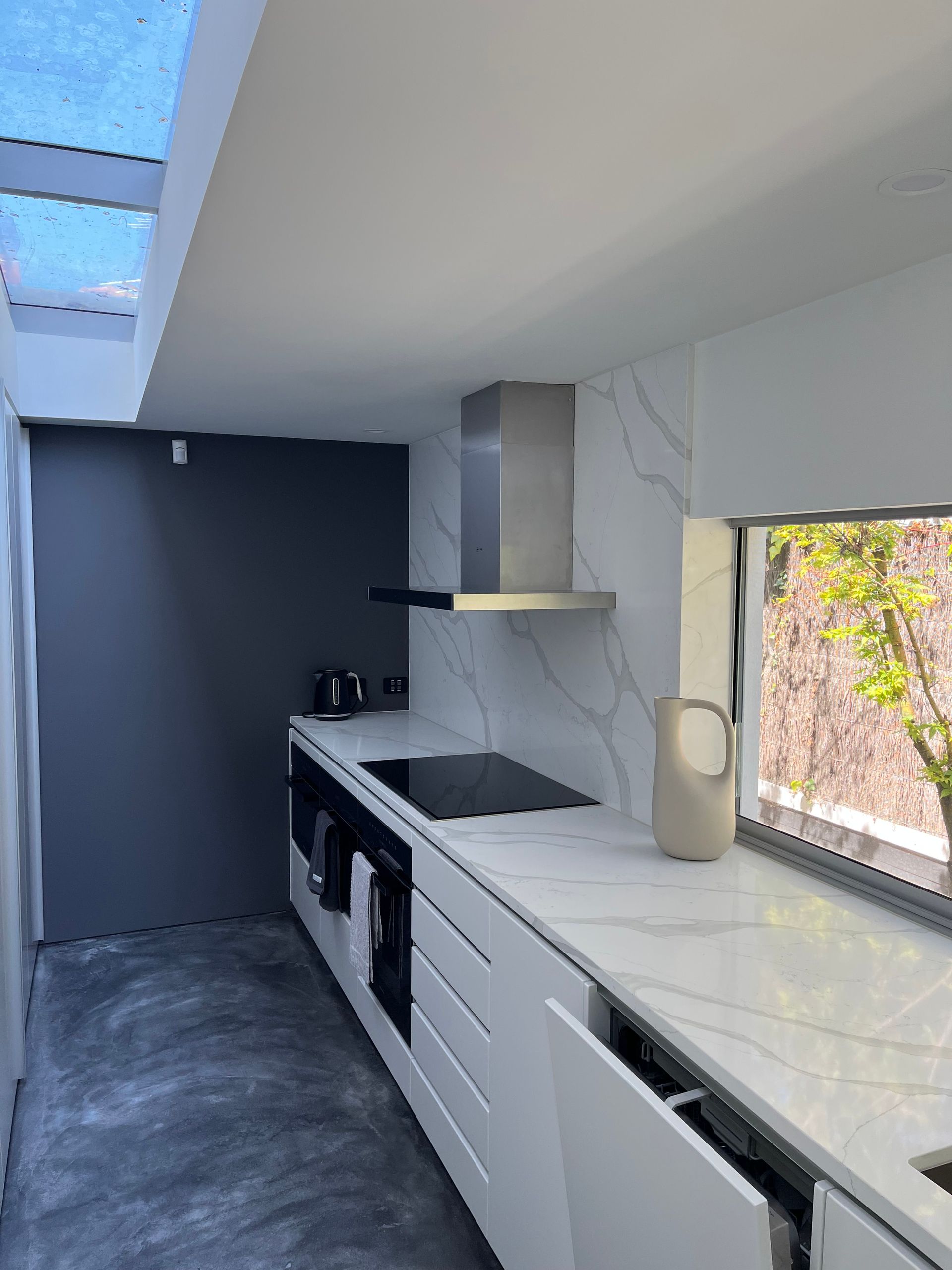 Modern white kitchen with gray accent wall, skylight, stainless steel hood, and marble countertops.