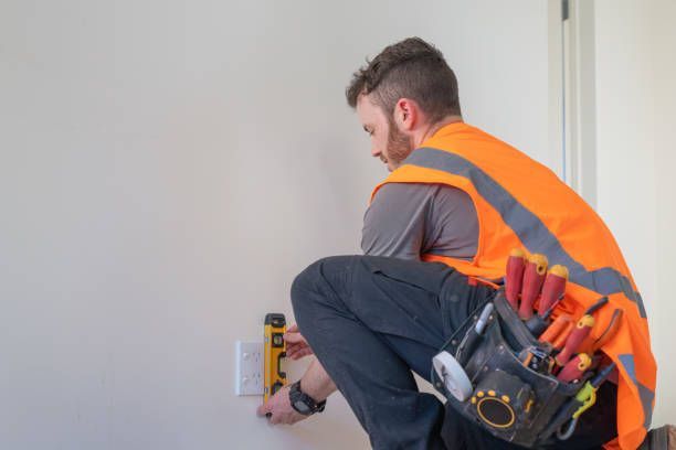 A man in an orange vest is kneeling down and working on a wall.