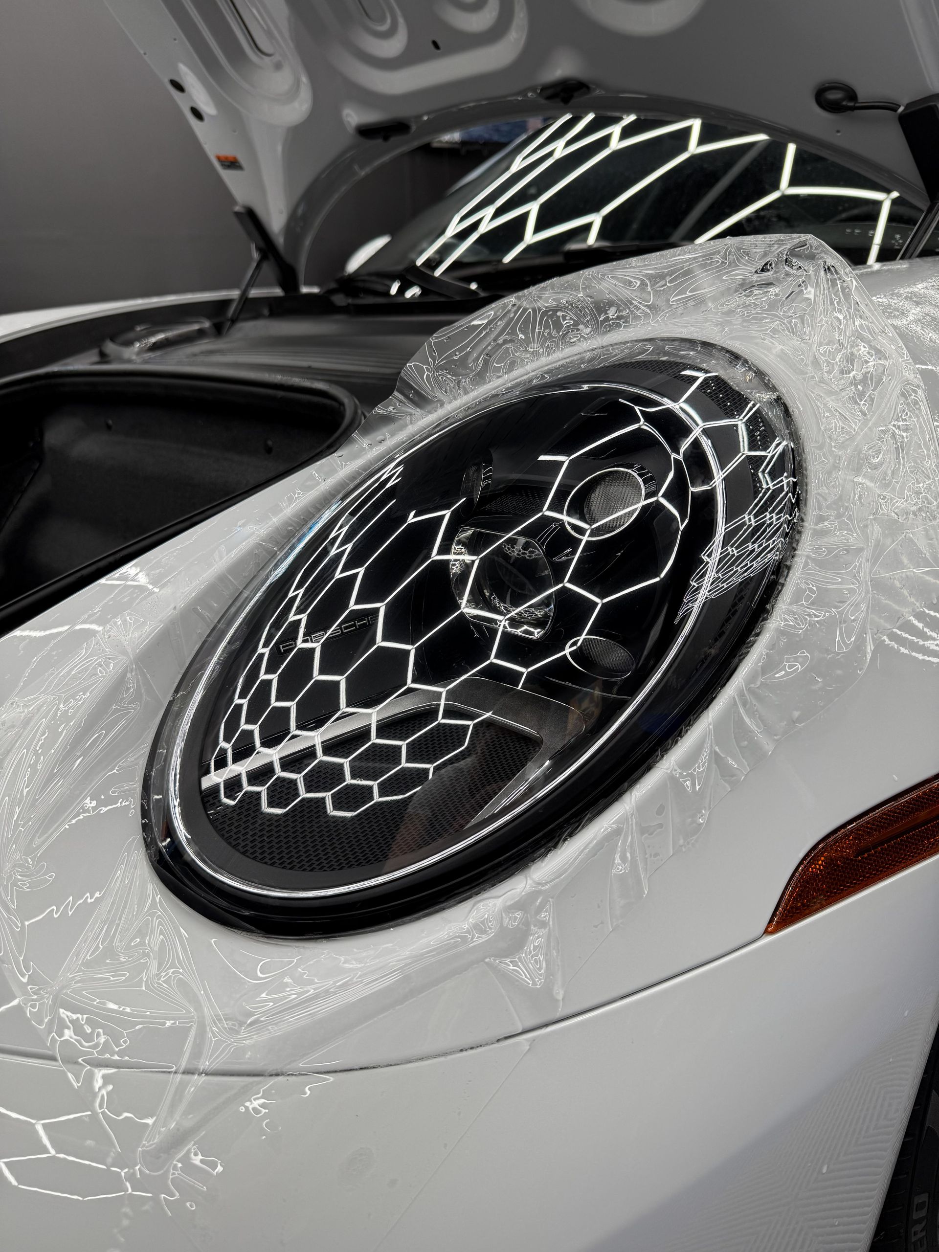 White Porsche headlight with a protective film applied, garage setting.