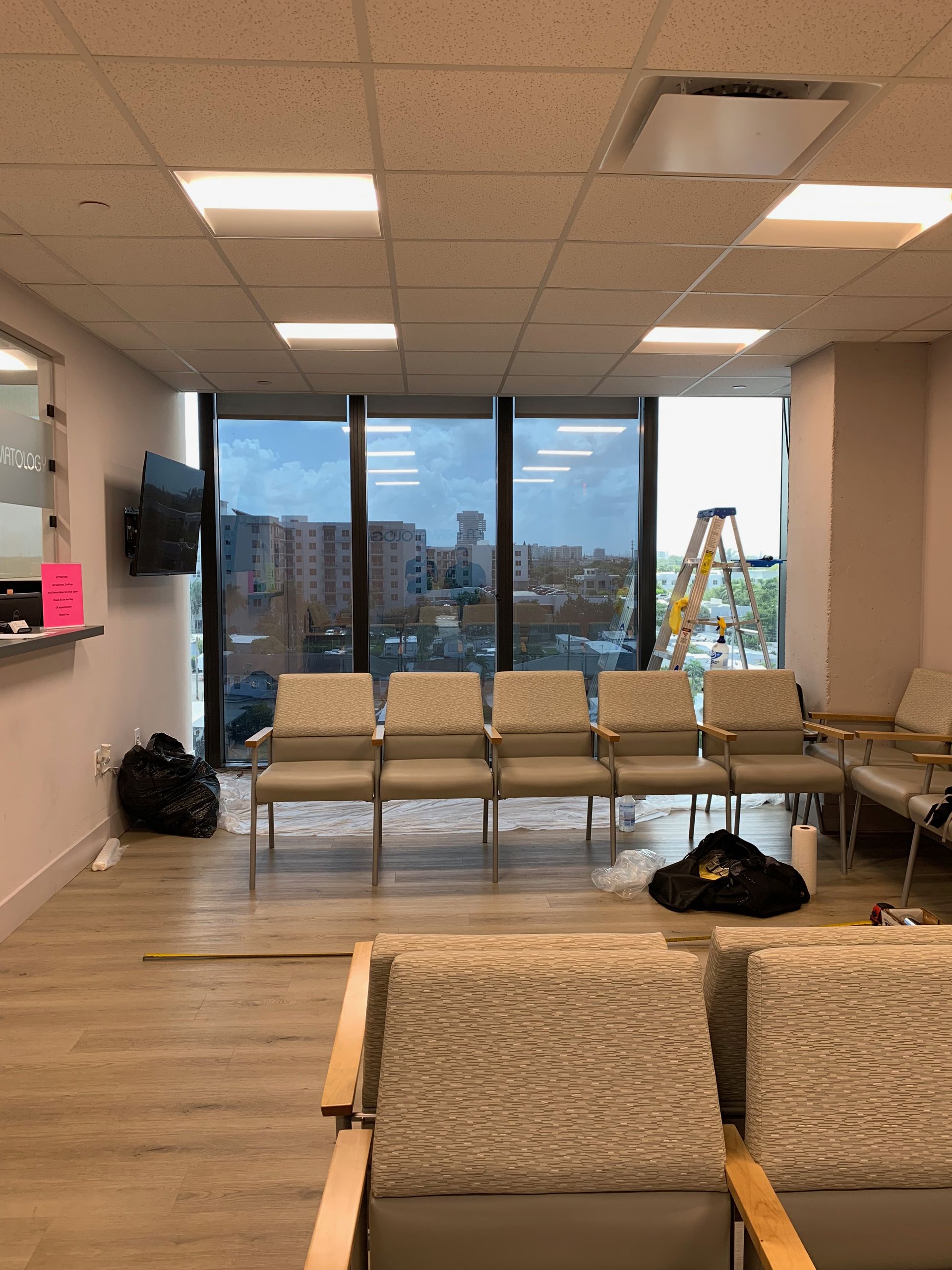 A waiting room with chairs, a window overlooking a cityscape, and a ladder.