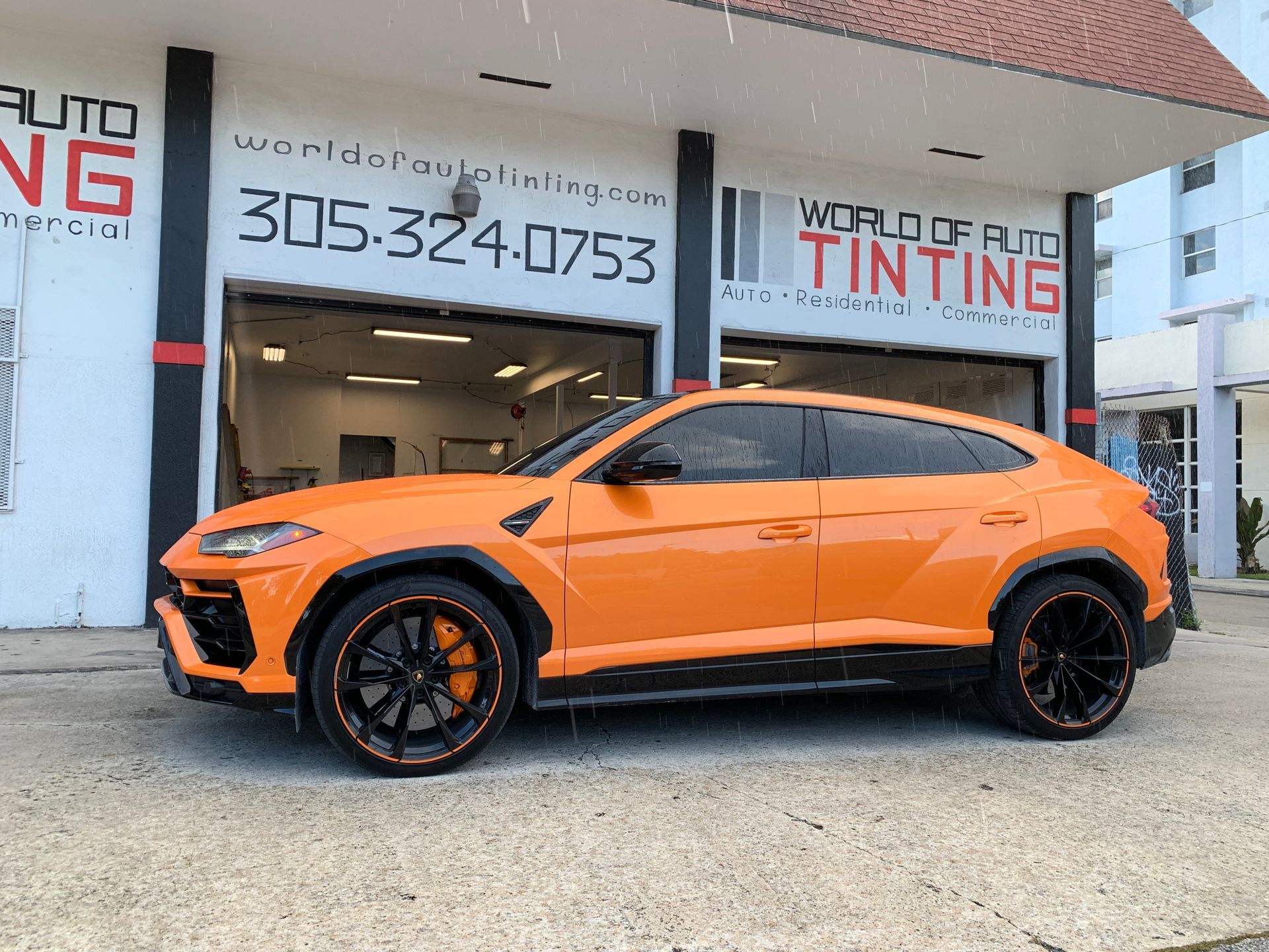 Orange Lamborghini SUV parked outside a car tinting shop.