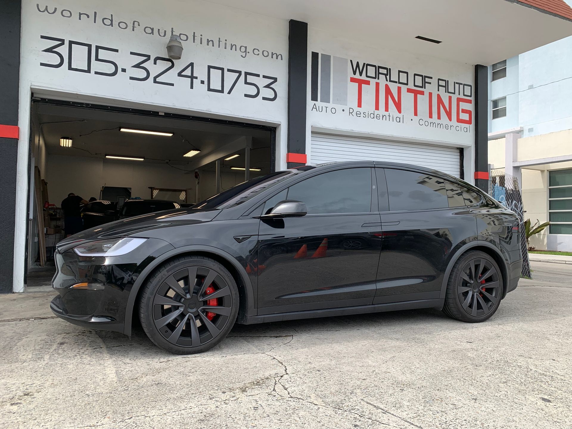 A black tesla model x is parked in front of a car tinting shop.