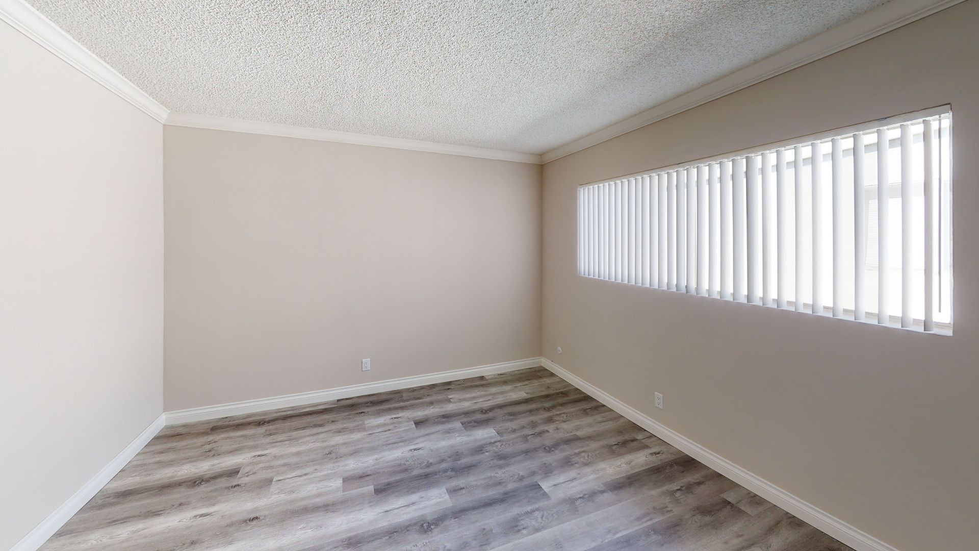 Empty room with wood-look floor, window with blinds, and light-colored walls.