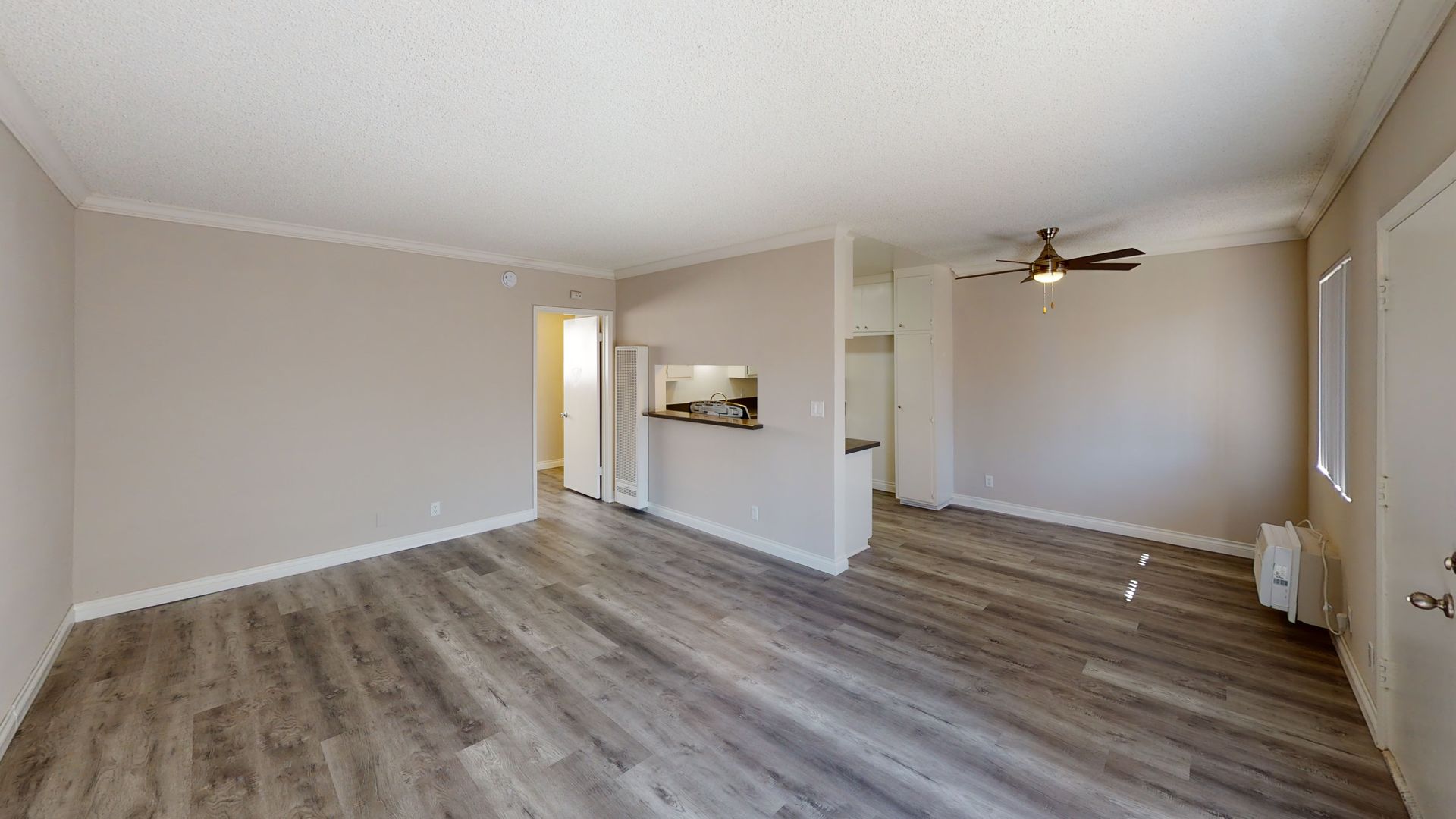 Empty apartment interior with light gray walls, wood-look flooring, and a ceiling fan.