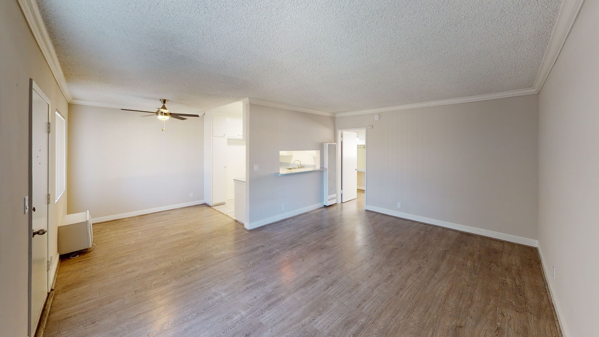 Empty living room with light brown wood-look flooring, white walls, and a ceiling fan.