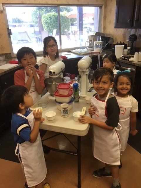 A group of children in aprons are standing around a table in a kitchen.