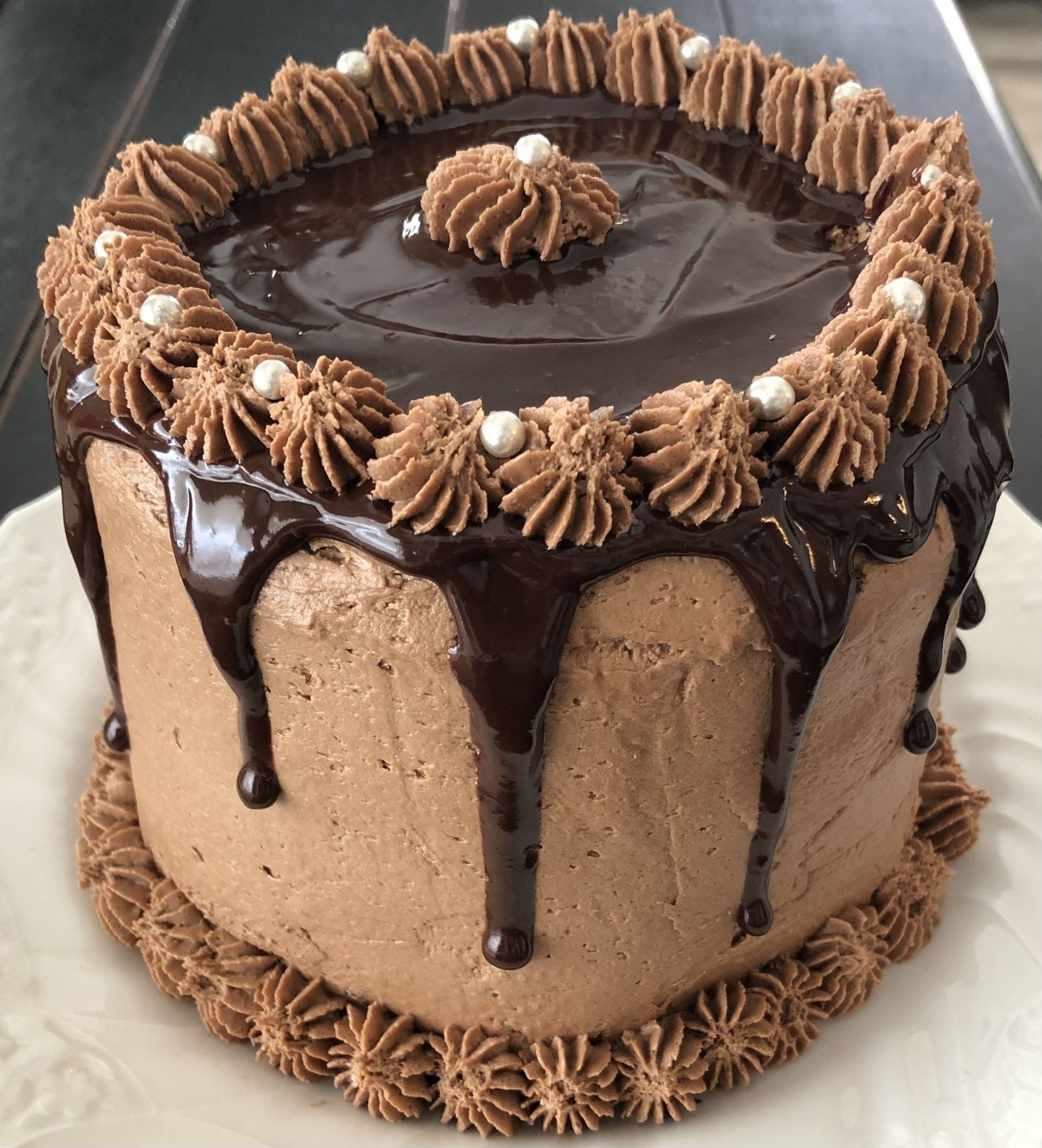 A chocolate cake with chocolate frosting and pearls on a white plate