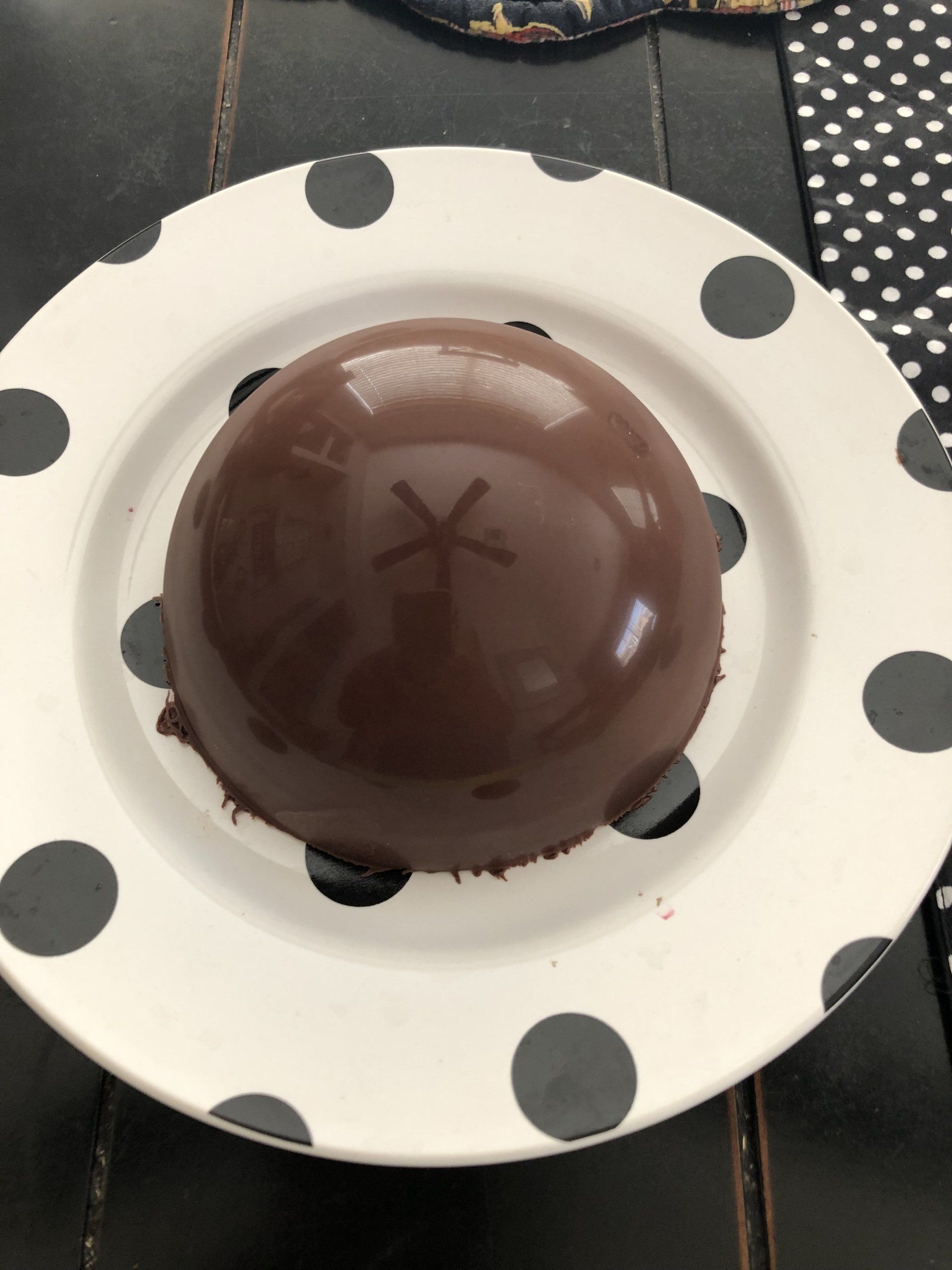 A white plate with black polka dots has a chocolate sphere on it