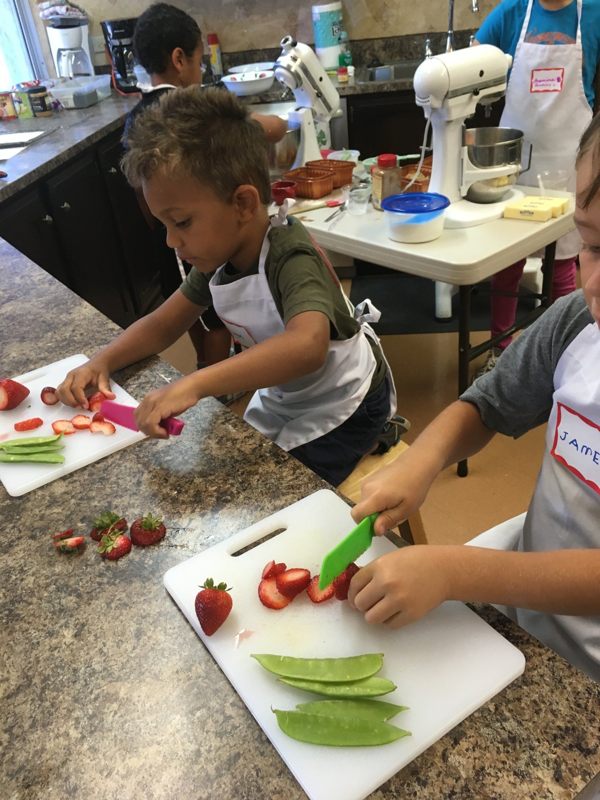 Two young boys are cutting strawberries and green peas on cutting boards