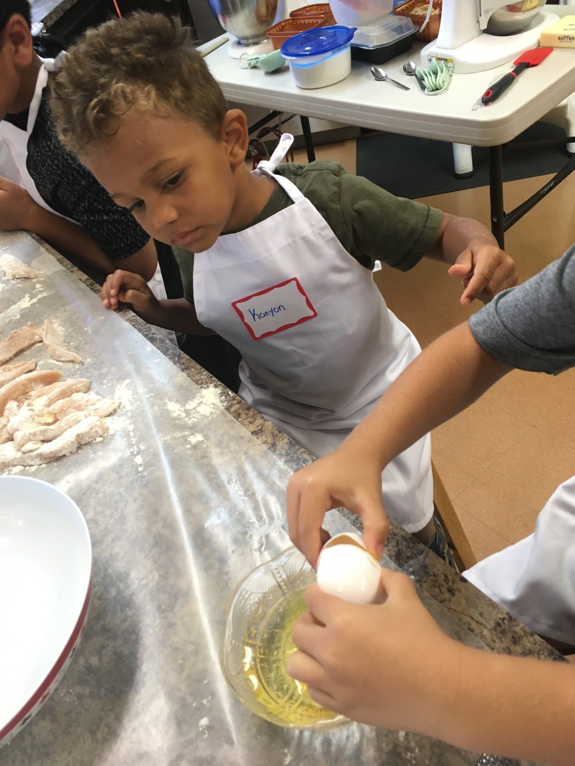 A young boy in an apron is cracking an egg into a bowl