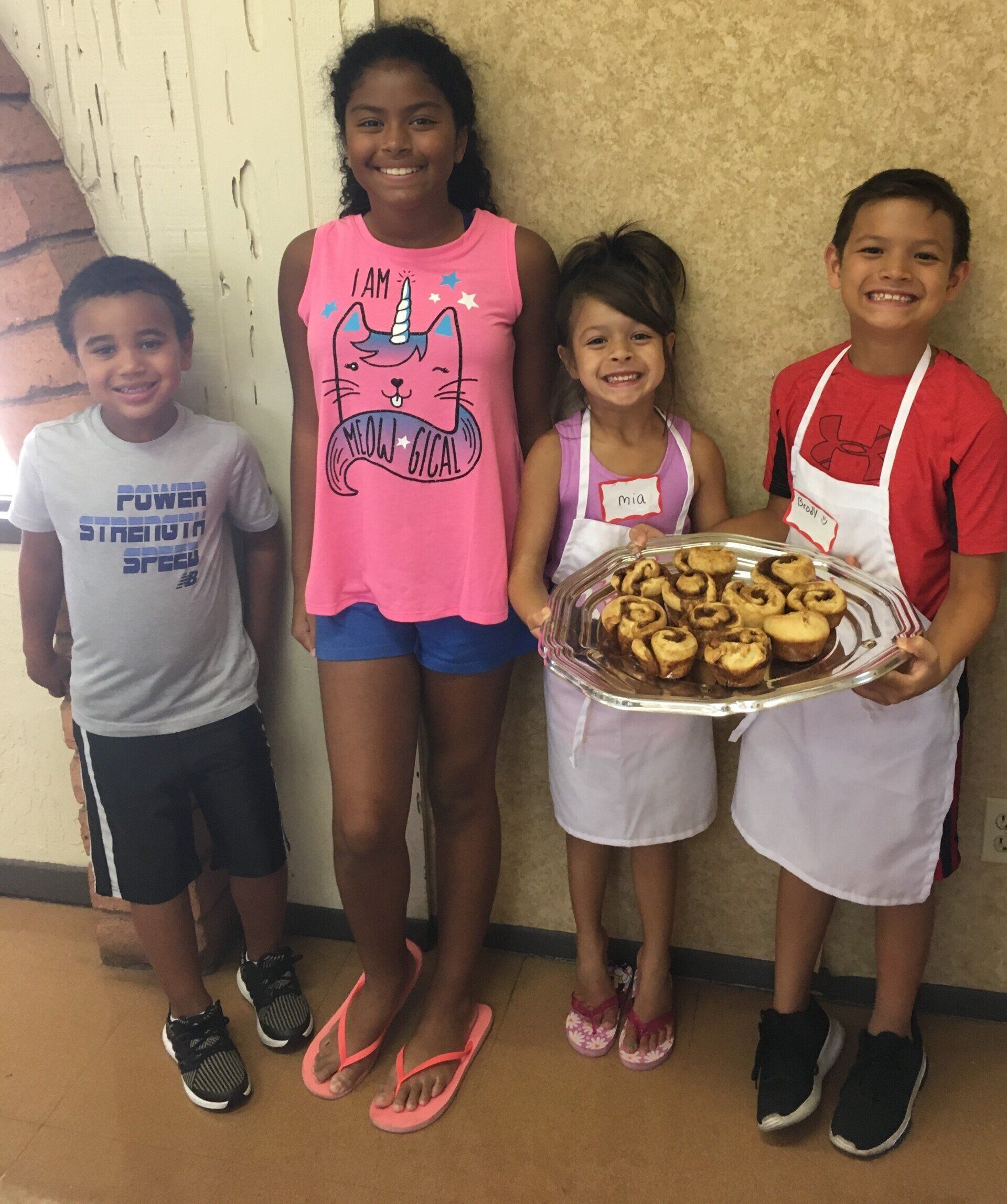 A girl in a pink tank top is holding a tray of cupcakes