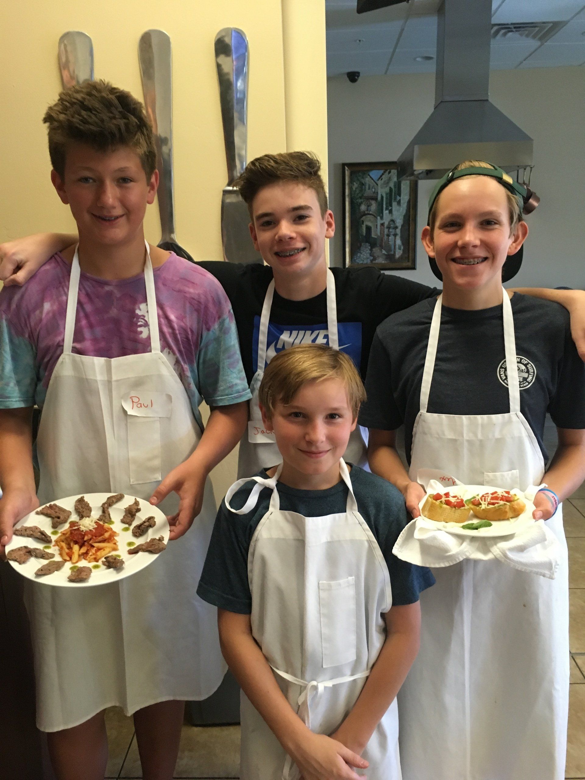A group of young people wearing aprons holding plates of food