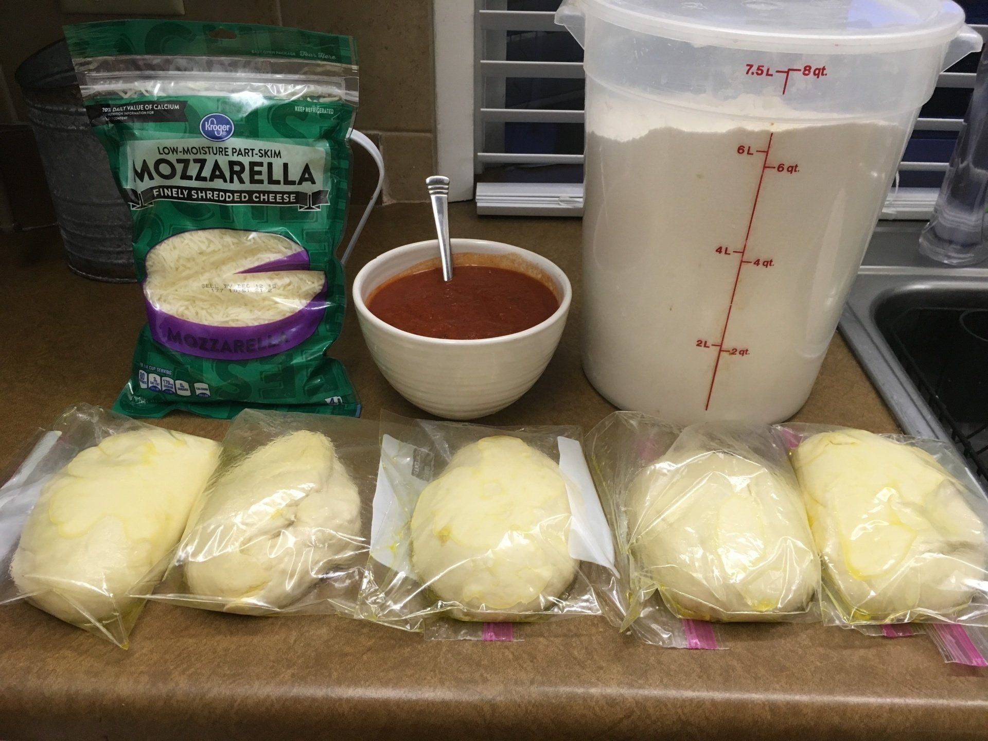 A bag of mozzarella cheese sits on a counter next to a bowl of sauce