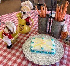 A table topped with a cake , carrots , and a pitcher.