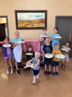 A group of children are standing in a room holding plates of food.