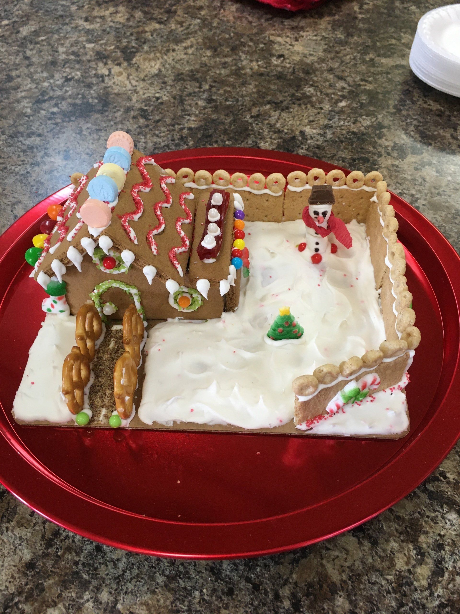 A gingerbread house is on a red plate on a table.