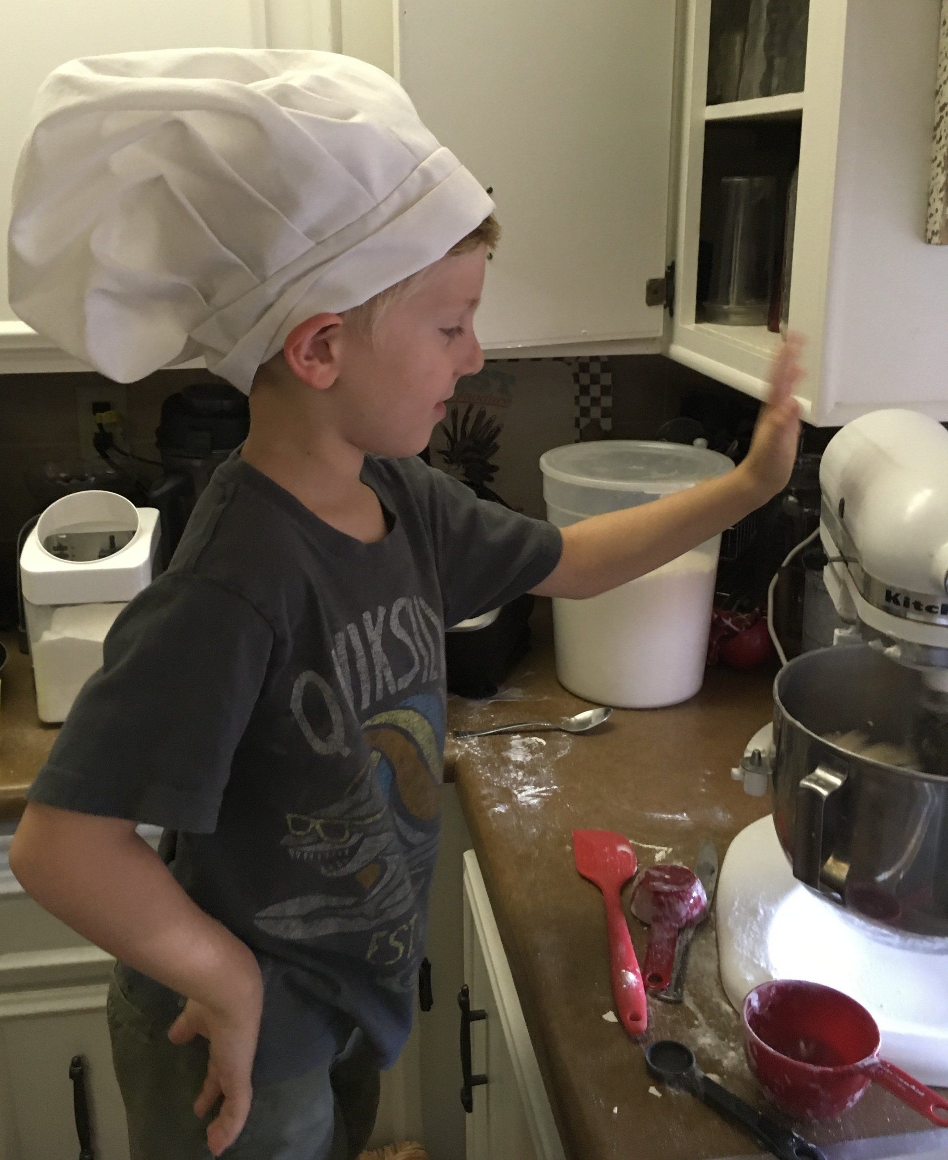 A young boy wearing a chef 's hat is standing in a kitchen