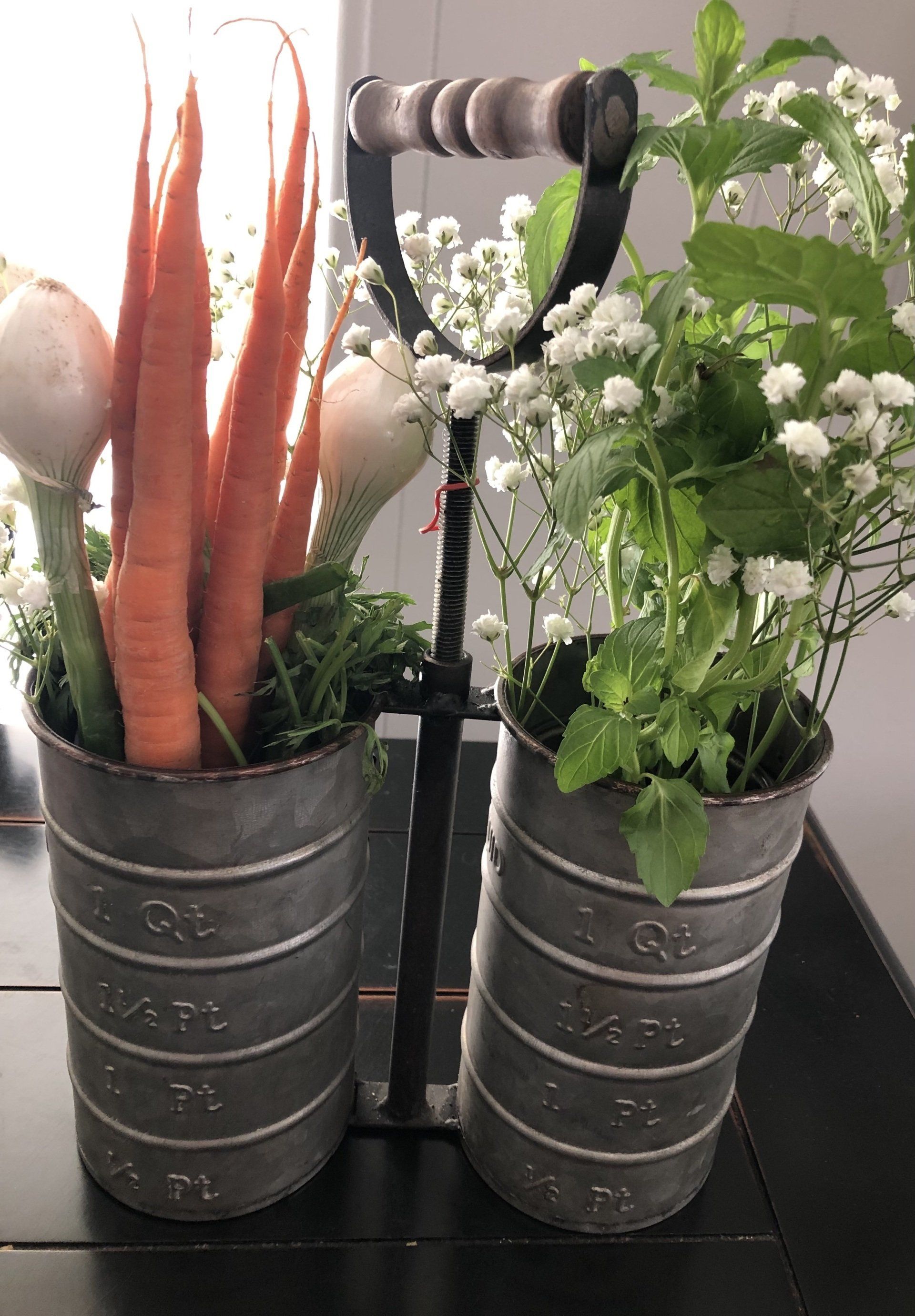 A couple of buckets filled with carrots and flowers on a table.