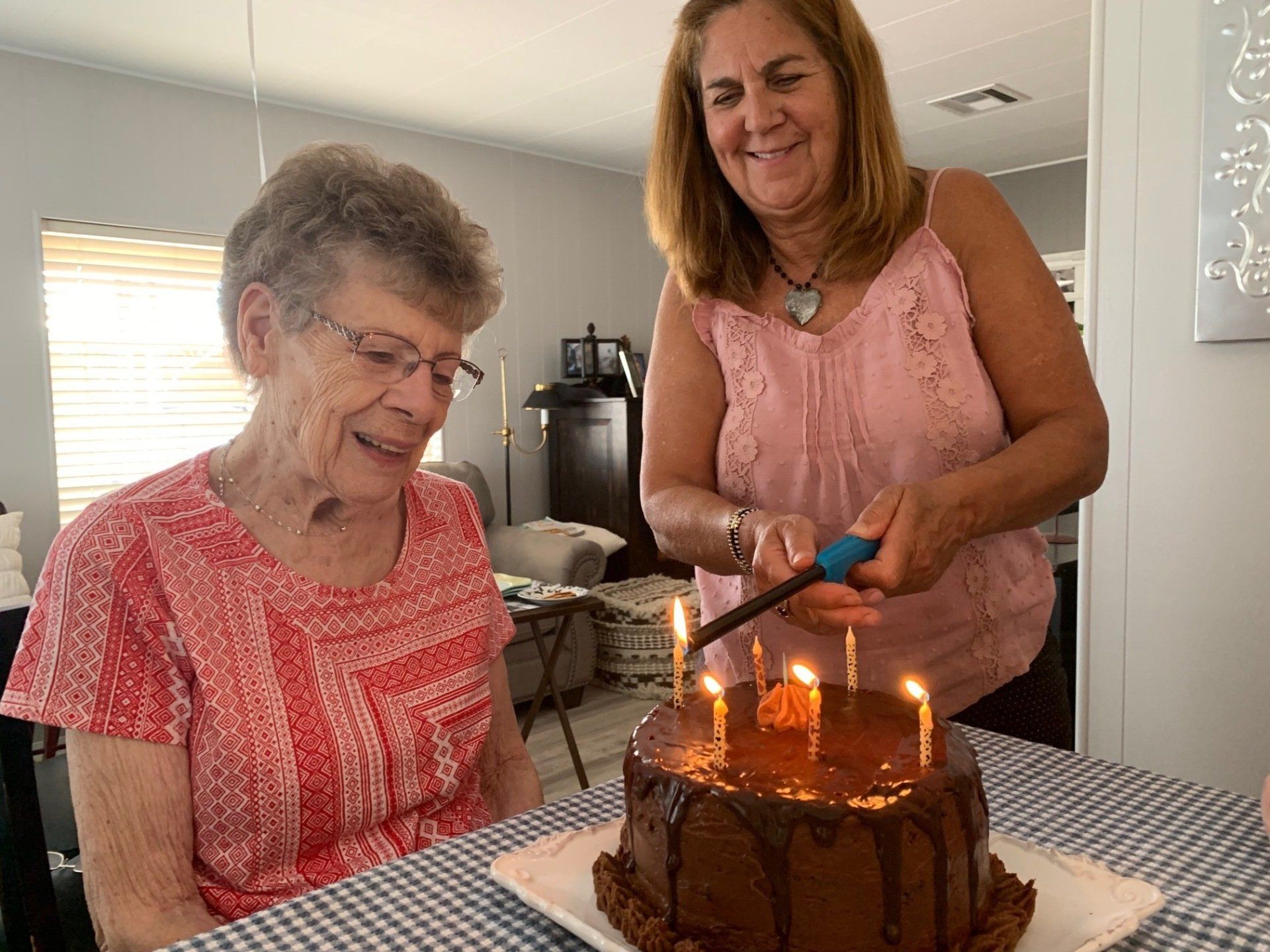 Two women are cutting a chocolate birthday cake with candles.