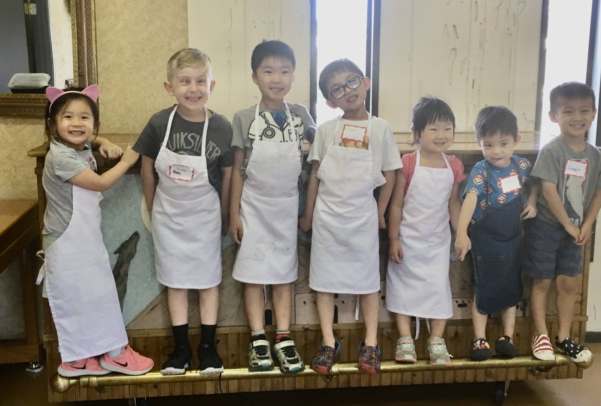 A group of children wearing aprons are standing next to each other.