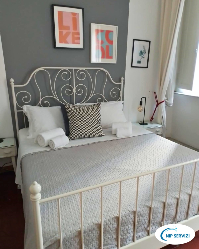 Letto bianco in ferro battuto in una camera da letto con pareti grigie, biancheria da letto bianca e quadri alle pareti.