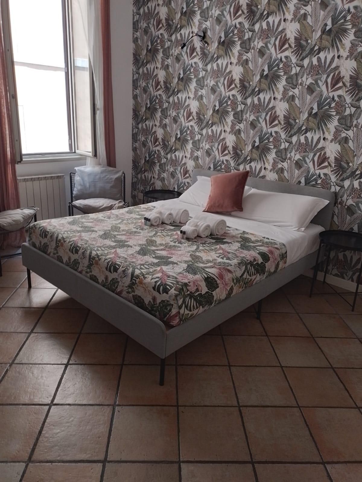 Camera da letto con letto, biancheria da letto floreale, carta da parati a fantasia e pavimento piastrellato.