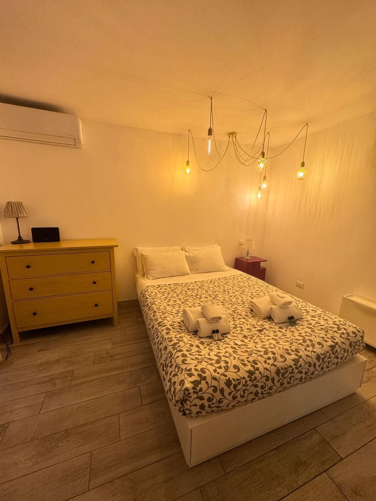 Camera da letto con letto, cassettiera gialla, luci sospese e aria condizionata.