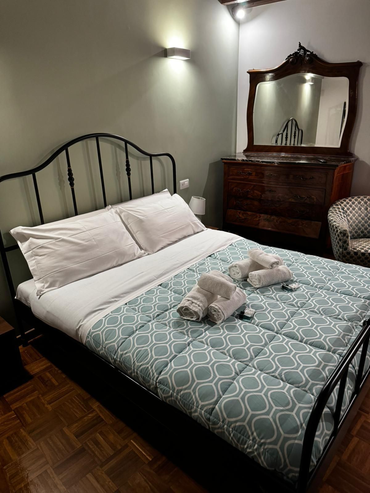 Camera da letto con letto in metallo nero, piumone blu fantasia, cassettiera in legno e poltrona.