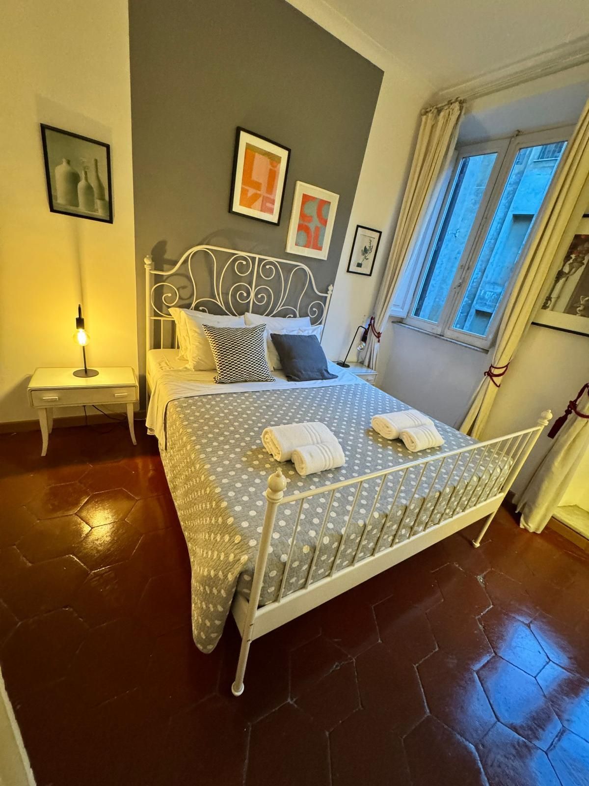 Camera da letto con letto bianco, piumone a pois, quadri incorniciati e una finestra. Combinazione di colori grigio e bianco.