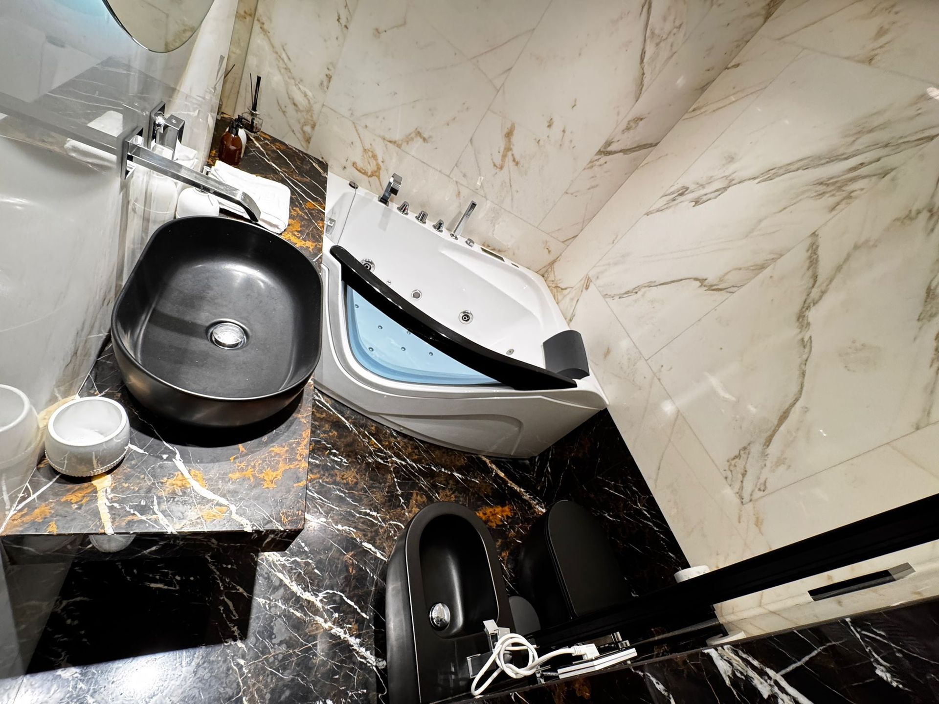 Bagno con lavandino, vasca e WC neri; superfici con motivi neri e dorati; pareti in marmo.